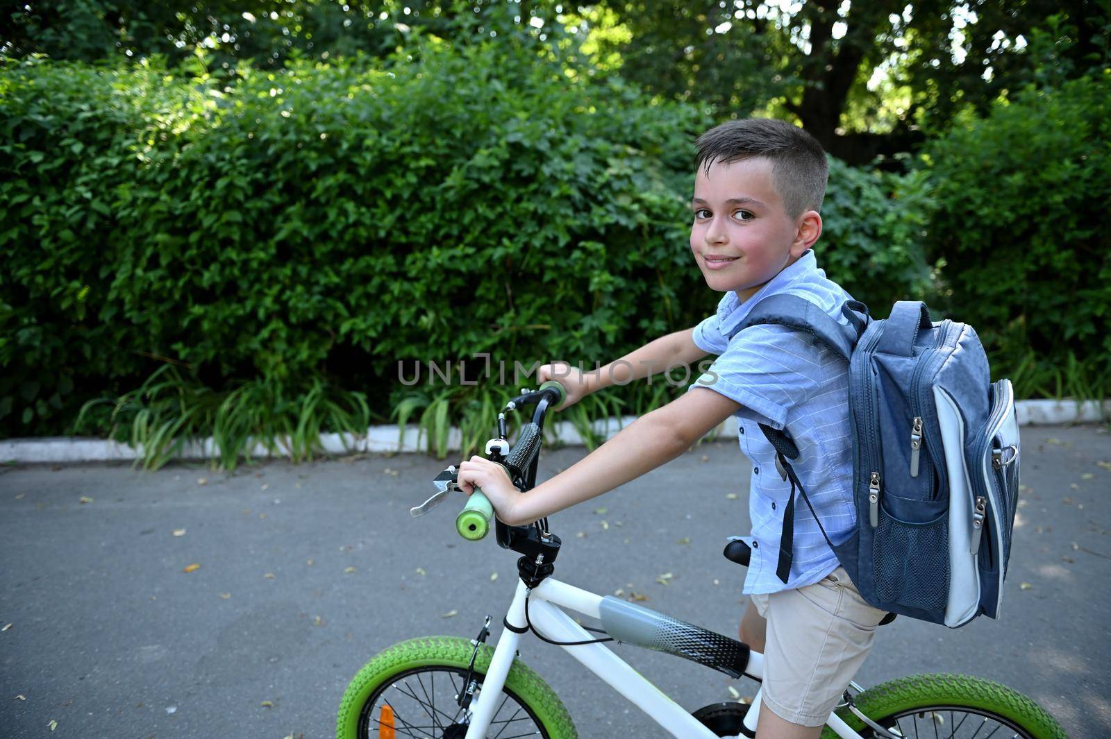 Adorable kid boy with school bag , riding a bicycle cute smiles looking at camera. Back to school concept