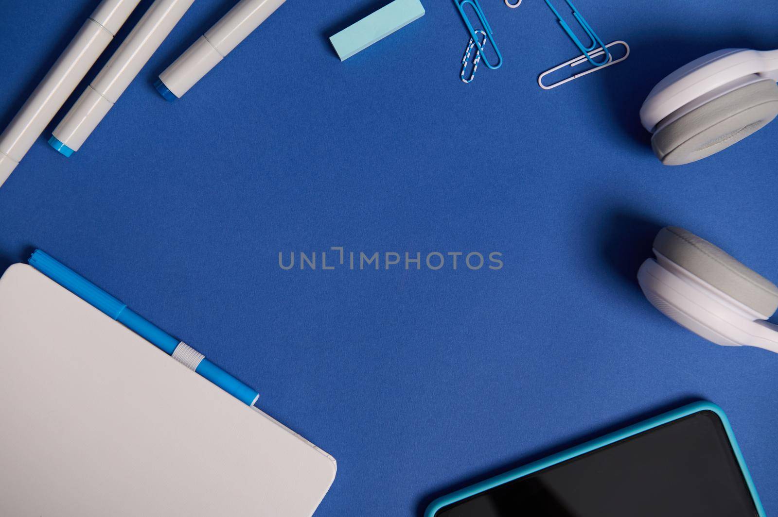 Flat lay composition with white stationery office or school supplies and electronic wireless gadgets scattered in a circle on blue background with copy space. Teacher's Day, Back to school concept