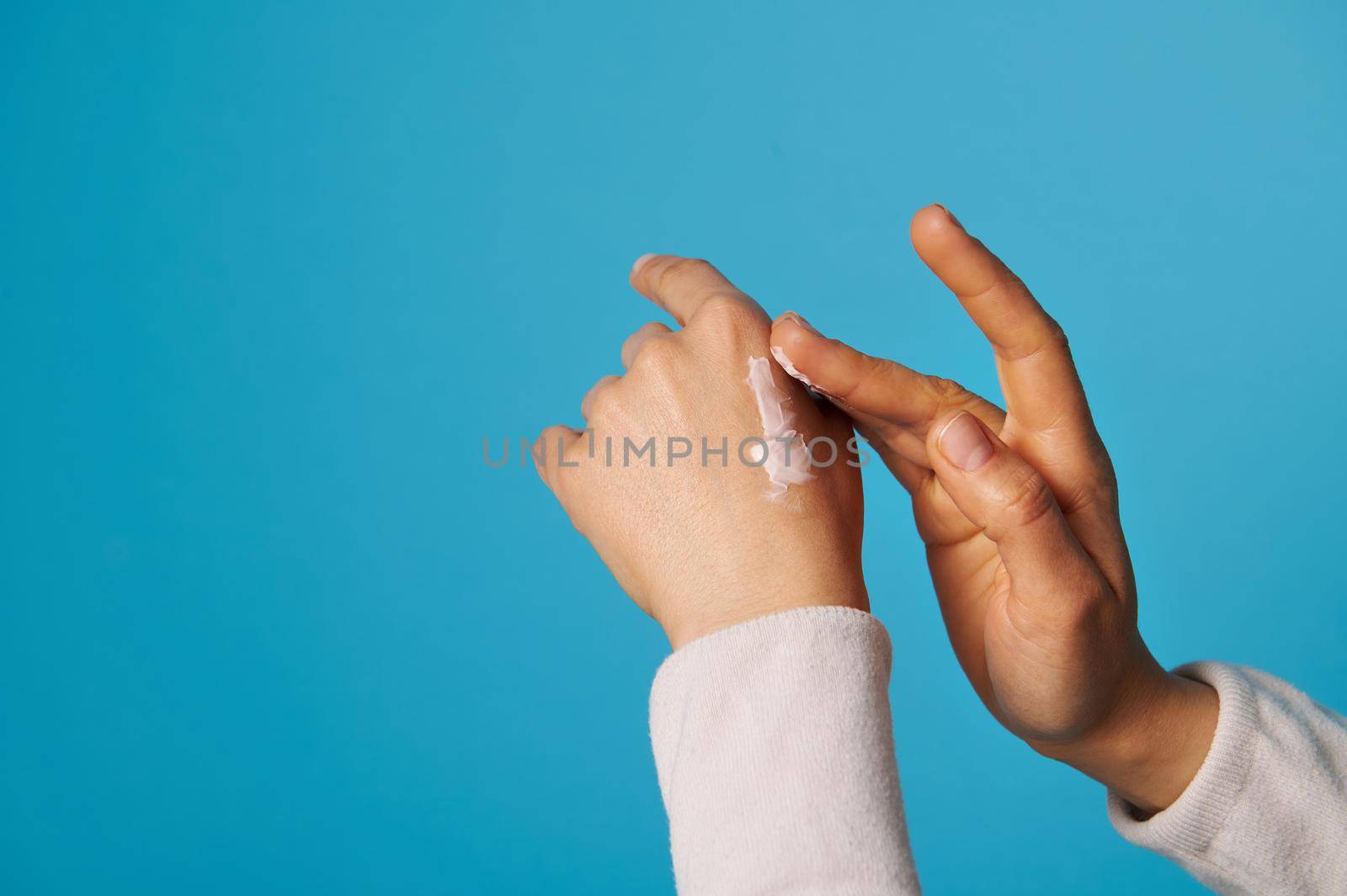 Closeup of woman's hands with moisturizing hand cream on blue background with copy space