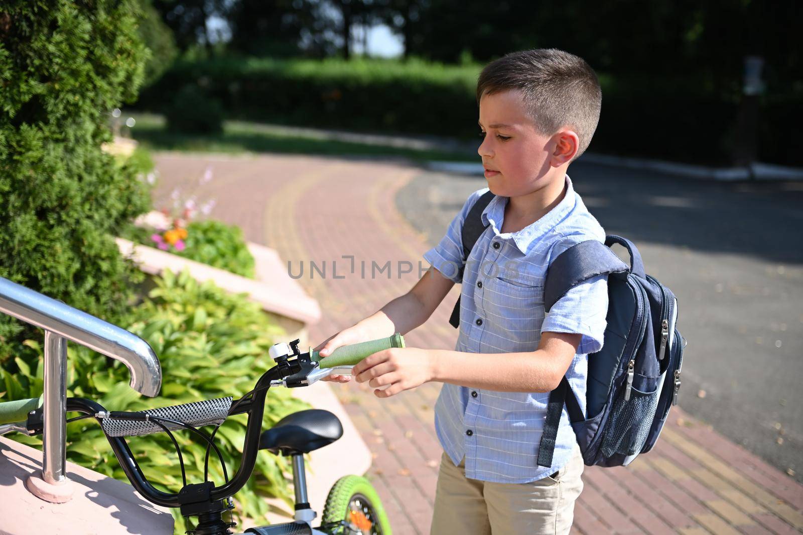 Adorable child parking his bike at school entrance. Handsome boy coming back to school
