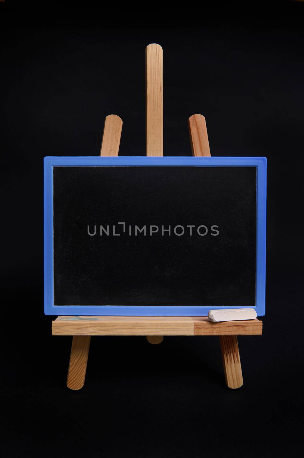 Close-up of a chalk board with empty space for text, standing on a wooden table easel isolated on black background with copy space. by artgf