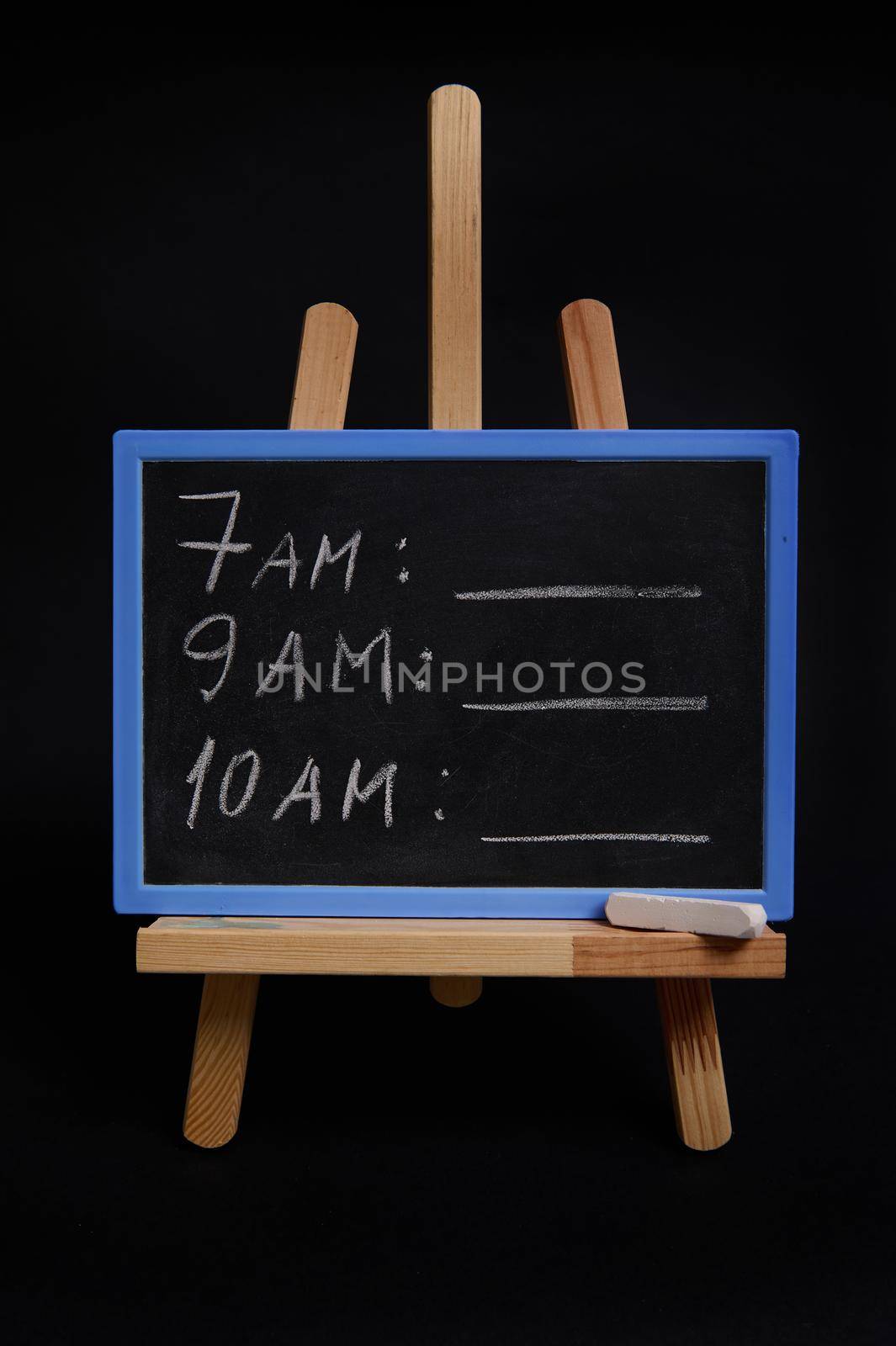 Lettering schedule with a white chalk, on a blackboard standing on a wooden table easel, isolated over black background with copy space. Planning concepts, time management, timetable and timing. by artgf