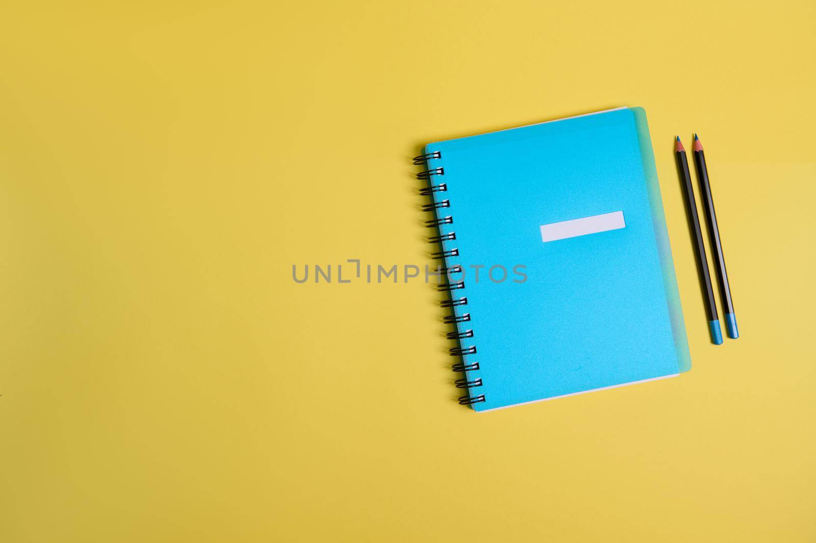 Blue colorful notepad, organizer and two pencils, on yellow background with space for text. Back to School and Teachers' Day, office and business, time management, planning concepts. Flat lay