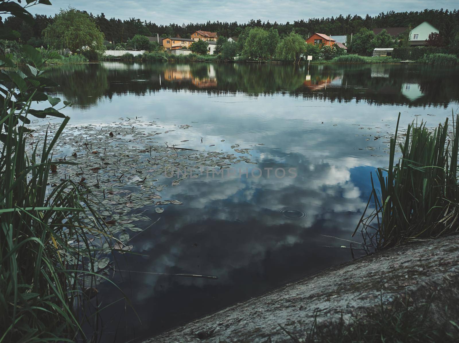 View of suburban residential houses from the opposite shore of the lake. Sky and clouds reflection on the river water