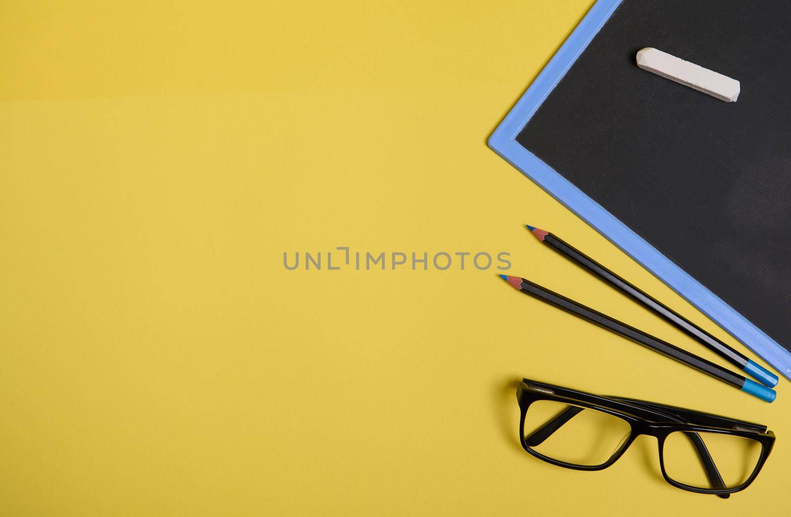 Flat lay composition. Chalk on a clean blackboard with copy space , eyeglasses and two pencils, isolated on yellow background with space for text by artgf