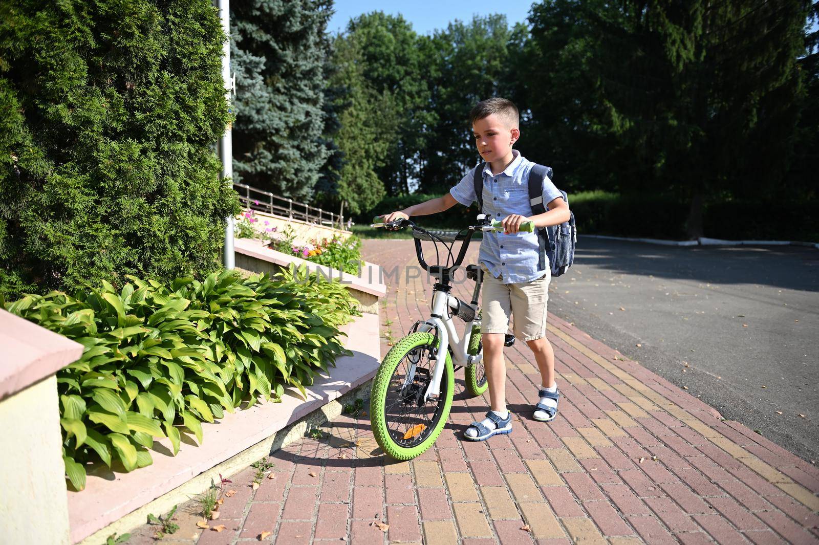 Full-length portrait of adorable child parking his bike at school entrance. Handsome boy coming back to school by artgf