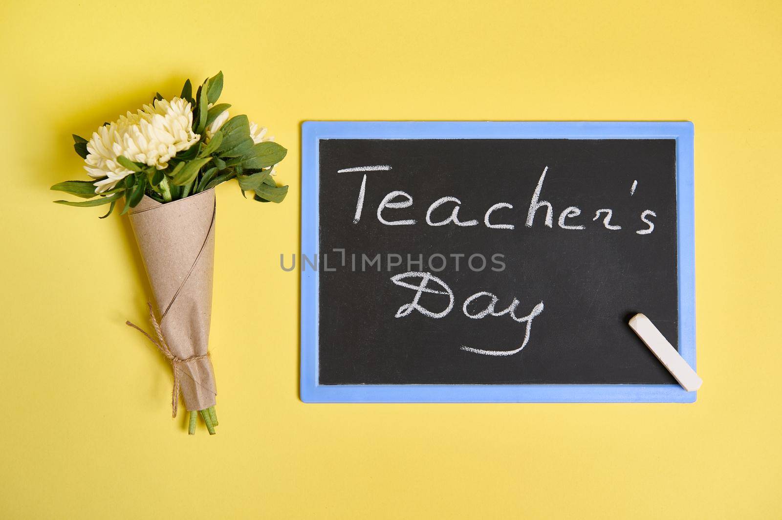 Flat lay composition of a beautiful bouquet of autumn asters flowers in craft wrapping paper tied with a rope and blackboard with inscription Teachers Day on yellow background with space for text