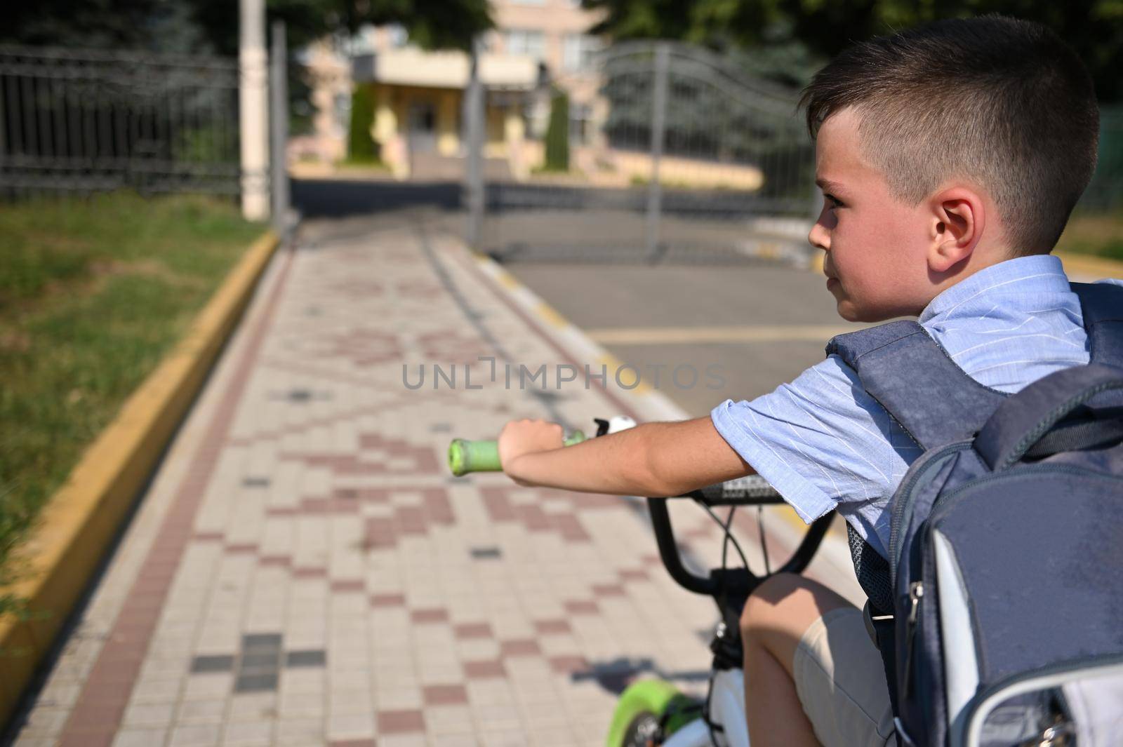 Portrait of handsome school boy with school bag riding bicycle to school establishment . Child coming back to school by artgf