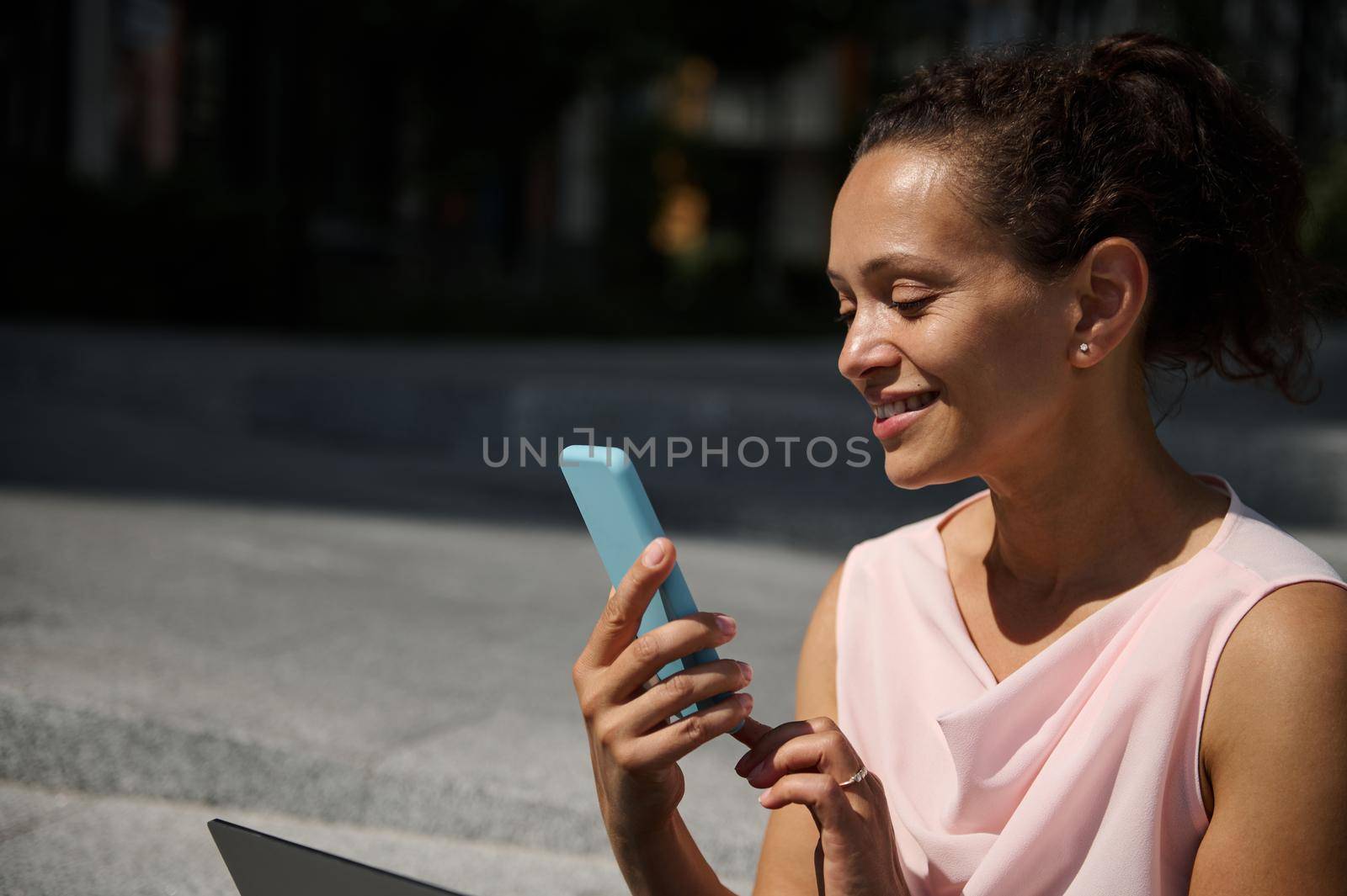 Attractive smiling African American woman swiping on smartphone. Attractive cheerful mixed race woman uses mobile phone outdoor