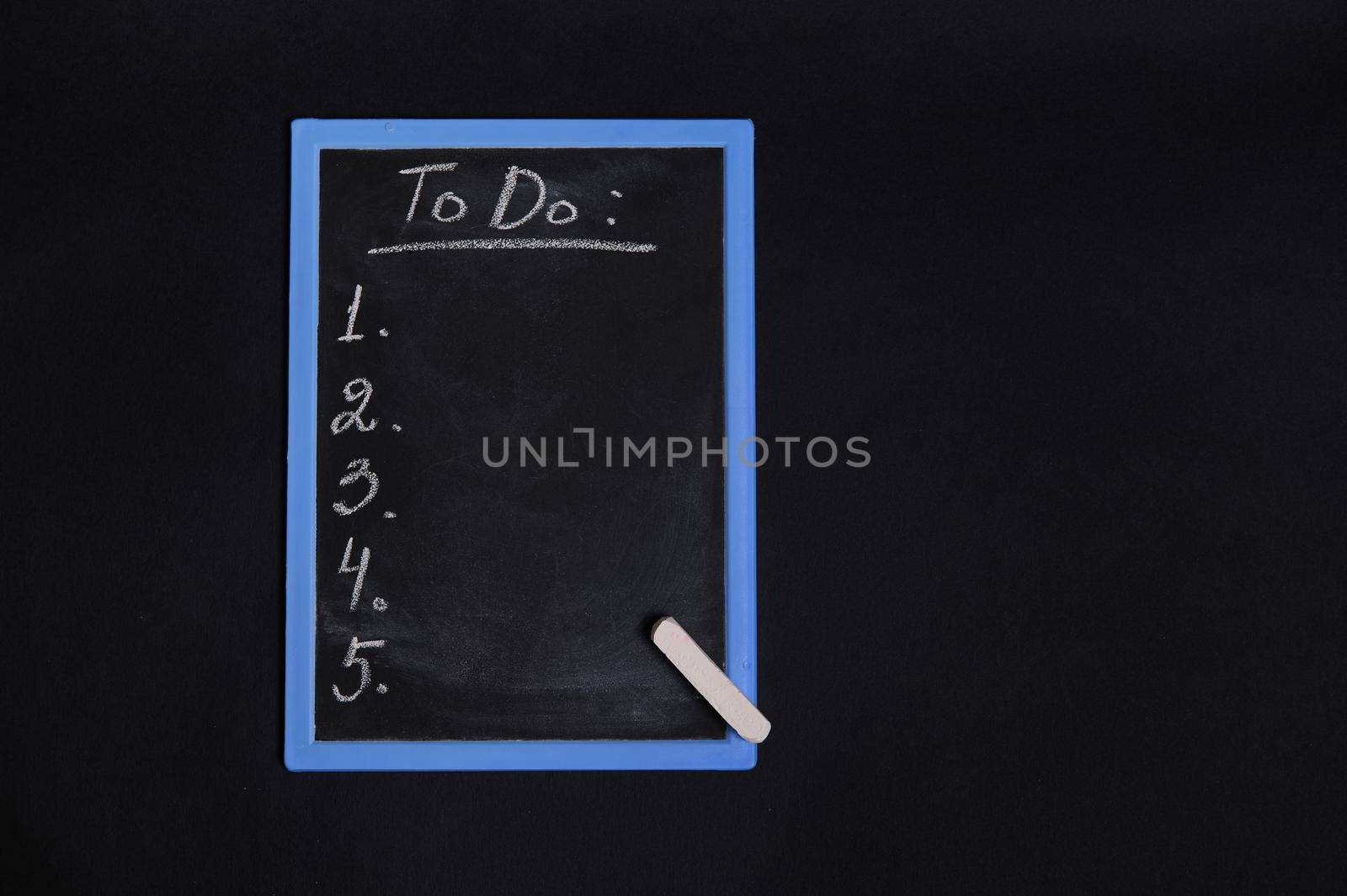 Flat lay of a chalkboard with lettering list to do, with empty copy space. Isolated on black background. Planning concepts, time management, timetable and timing.