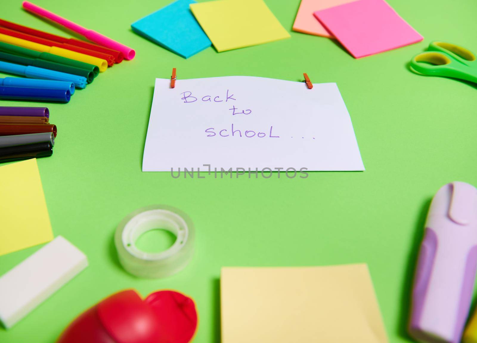 Soft focus on a white paper with lettering Back To School in the center of multi colored assortment of stationery office supplies and school accessories arranged in a circle. Copy space