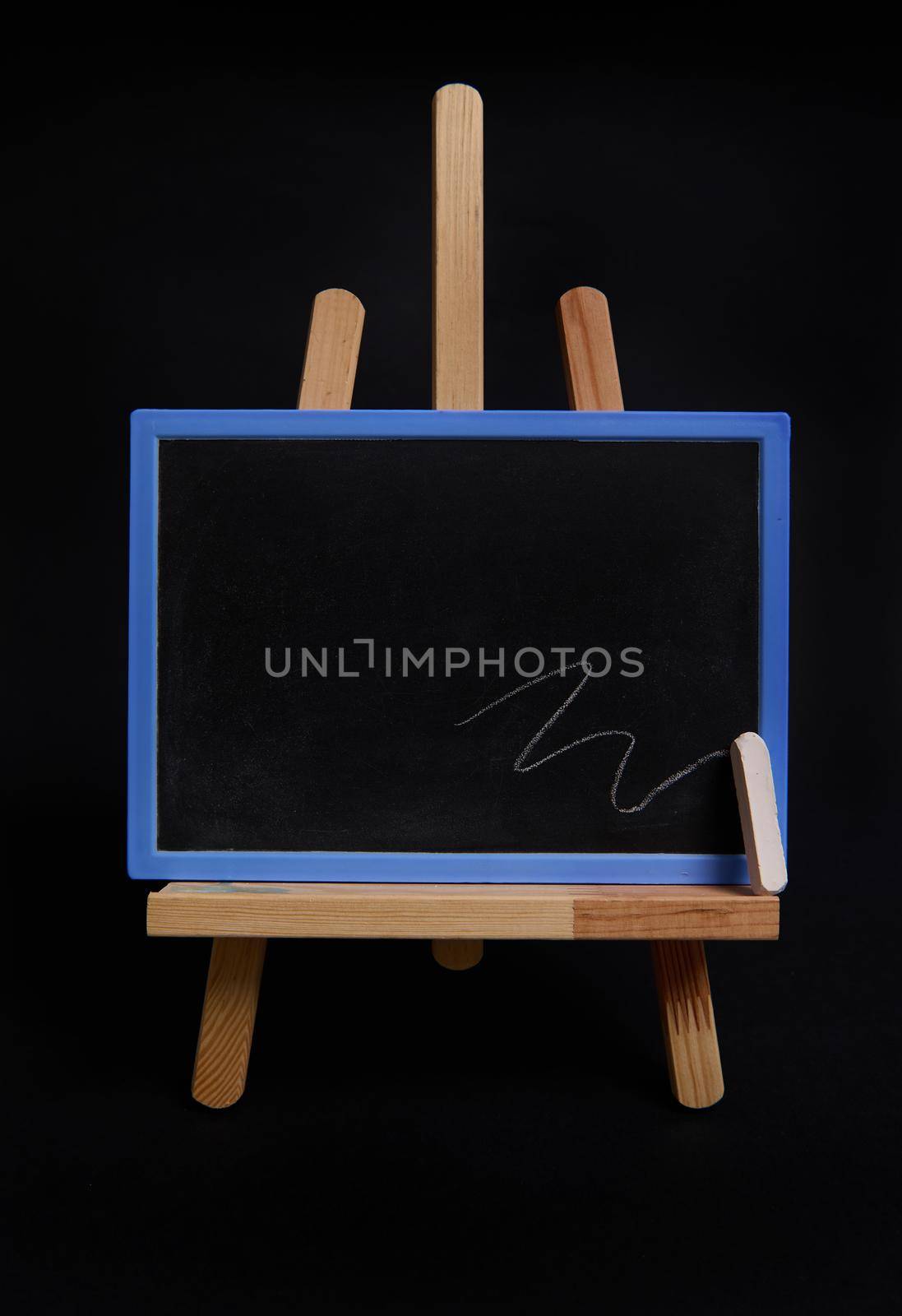 Close-up studio shot of a wooden table easel with a chalk and blackboard with empty blank space for text, isolated on black background by artgf