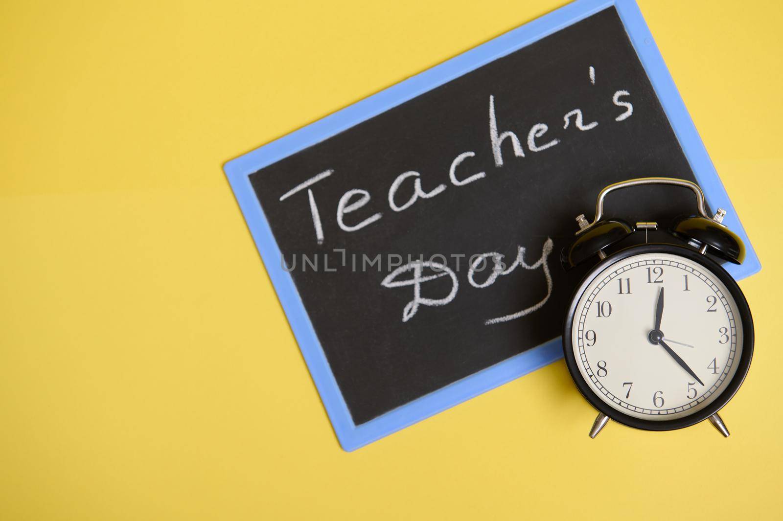 Flat lay composition from an alarm clock and chalkboard on yellow background with copy space for text. Teacher's Day