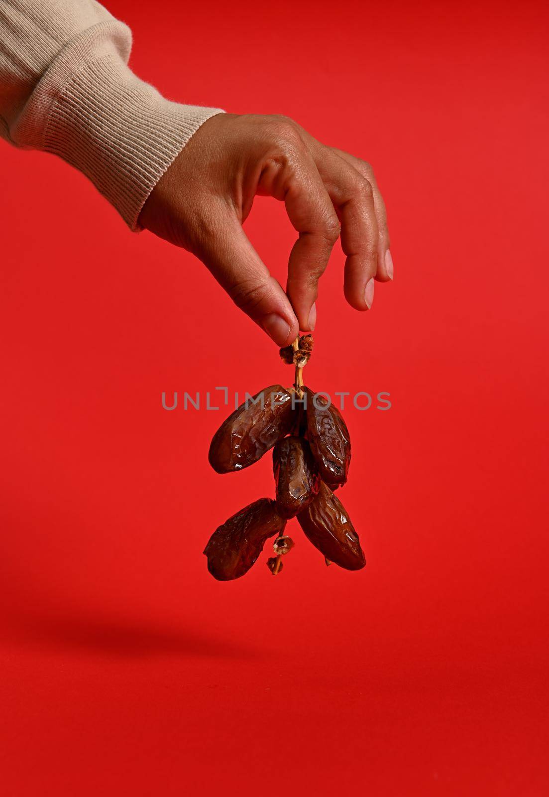 Close-up of hands holding a branch of fresh tasty sweet dates. Vertical shot on red background with copy space by artgf