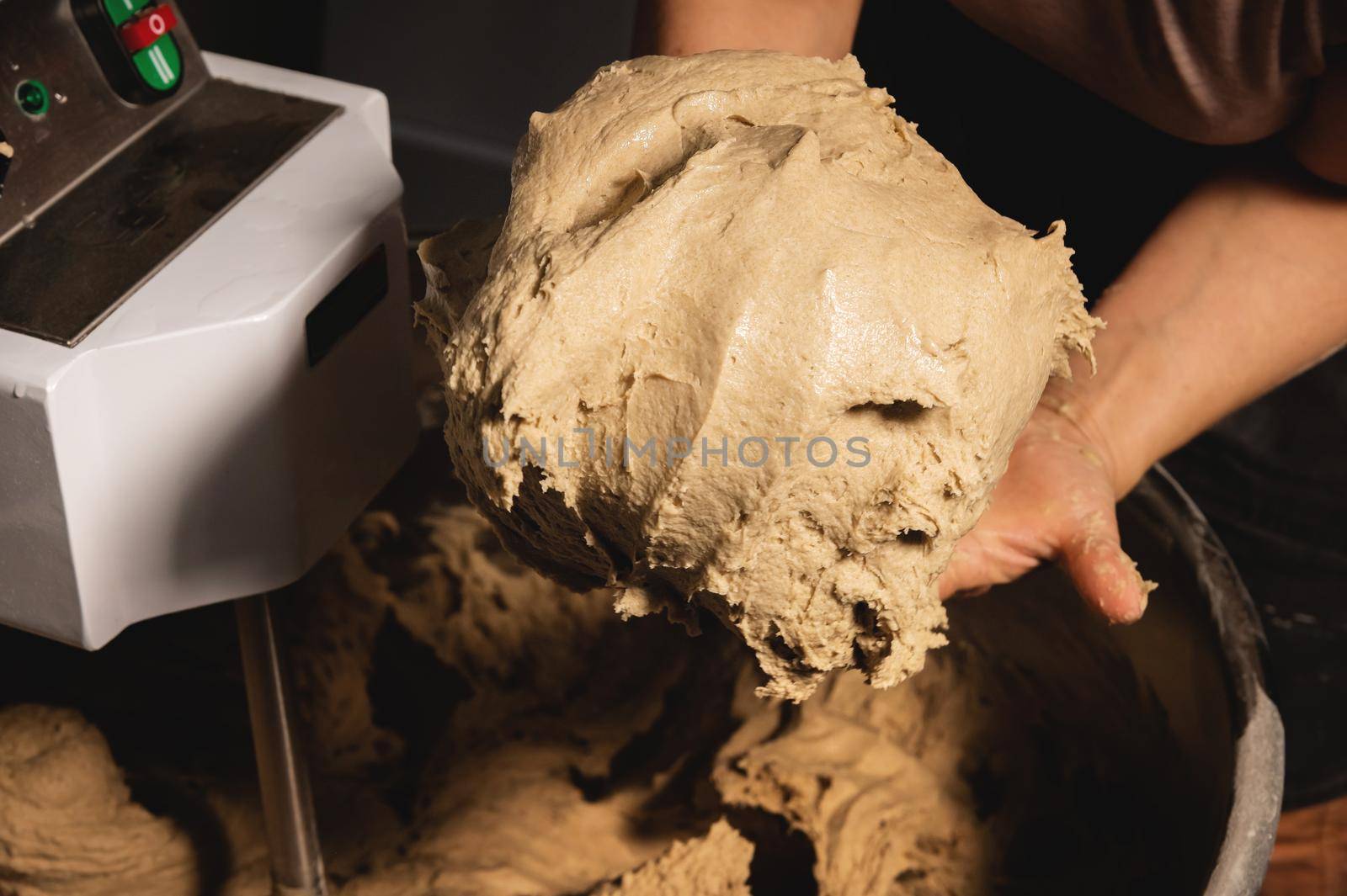 Close-up of baker's female hands holding dough against the background of a production dough mixer in a bakery.