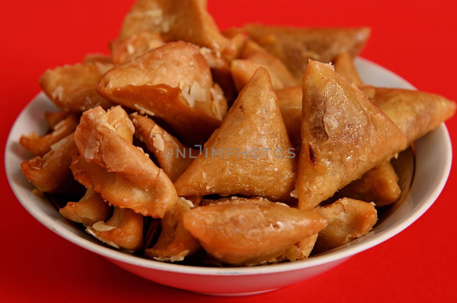 Close-up photography of delicious and sweet plate full of fresh traditional luxurious Moroccan handmade Brewat sweets, isolated on red background.