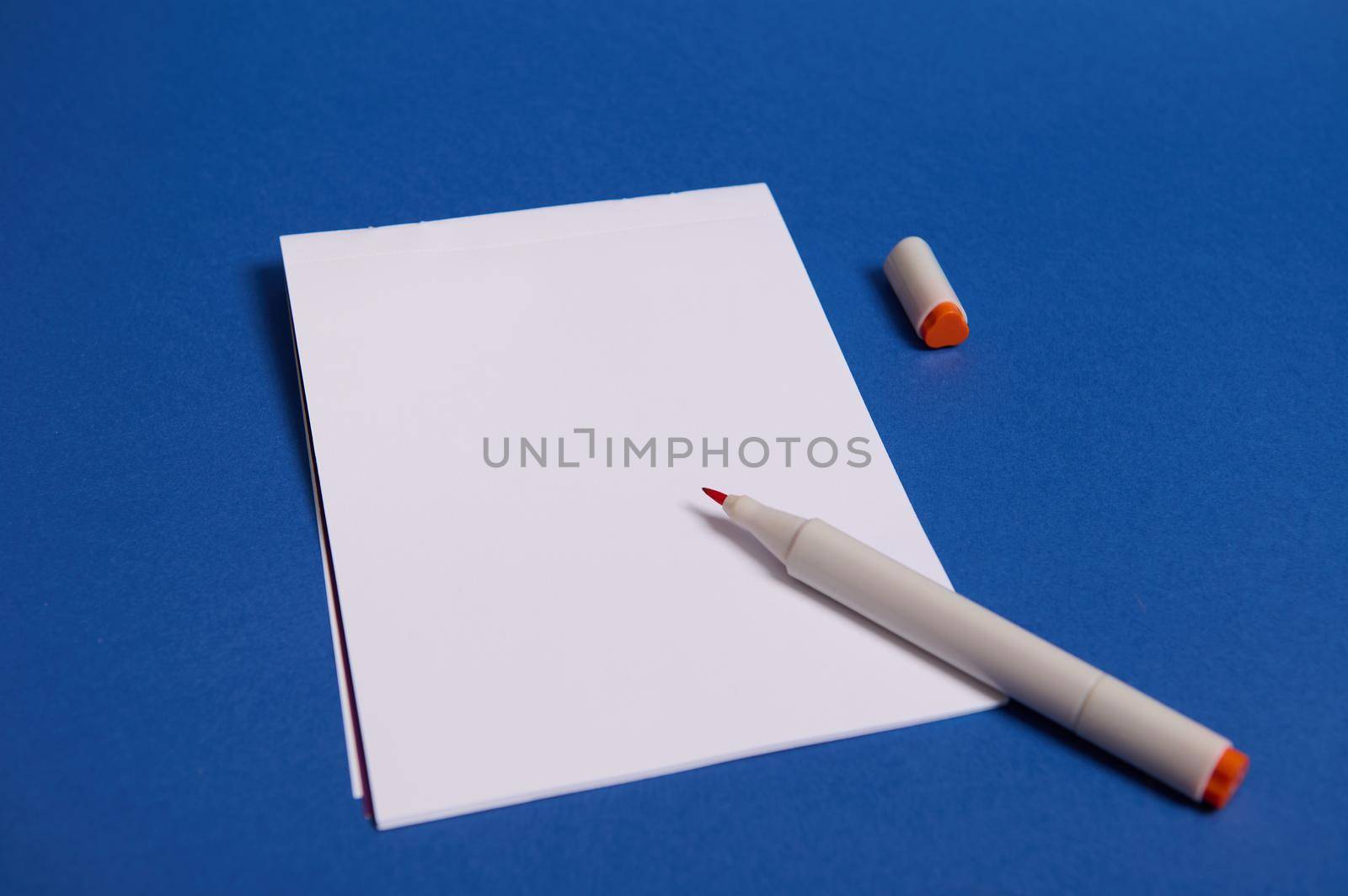 Top view of a composition with watercolor marker or felt-tip pens on white blank sheet of paper with copy space for text isolated on blue background.