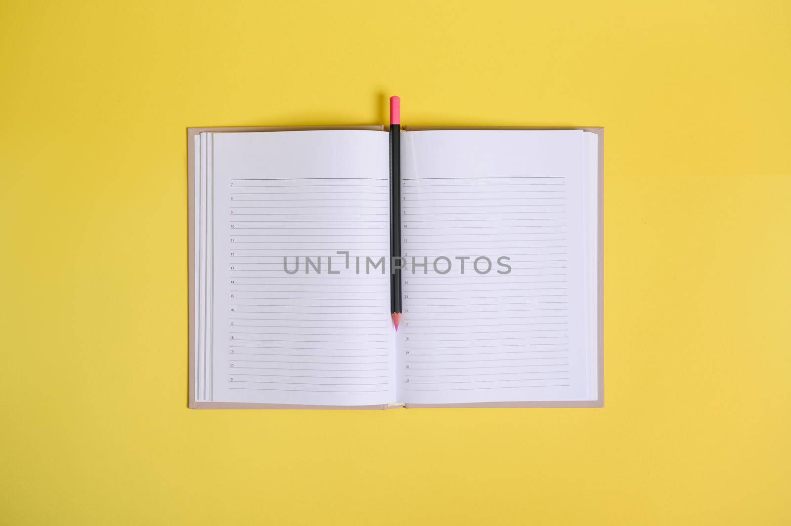 Flat lay composition on yellow background of a color pencil in the middle of an open organizer with clean blank white sheets with copy space.