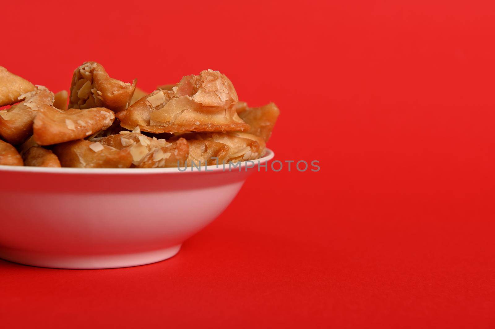 Isolated studio shot on red background of cropped plate with delicious Arabian Moroccan dessert for religious events on a plate. Copy space. Arabic traditional oriental sweets on the festive table