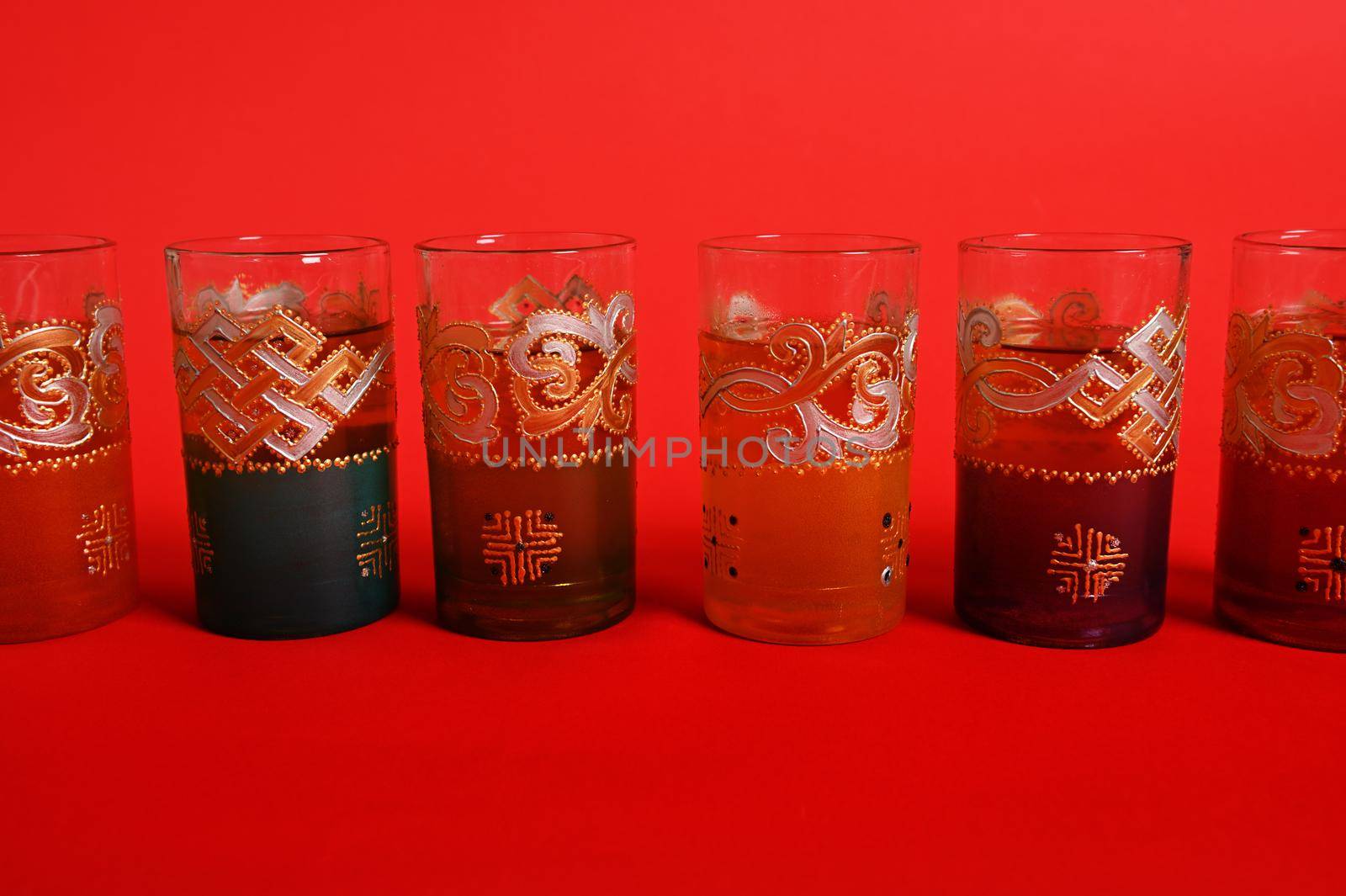 Multicolored glasses for Moroccan green mint tea, decorated in oriental style. Isolated on red background with copy space