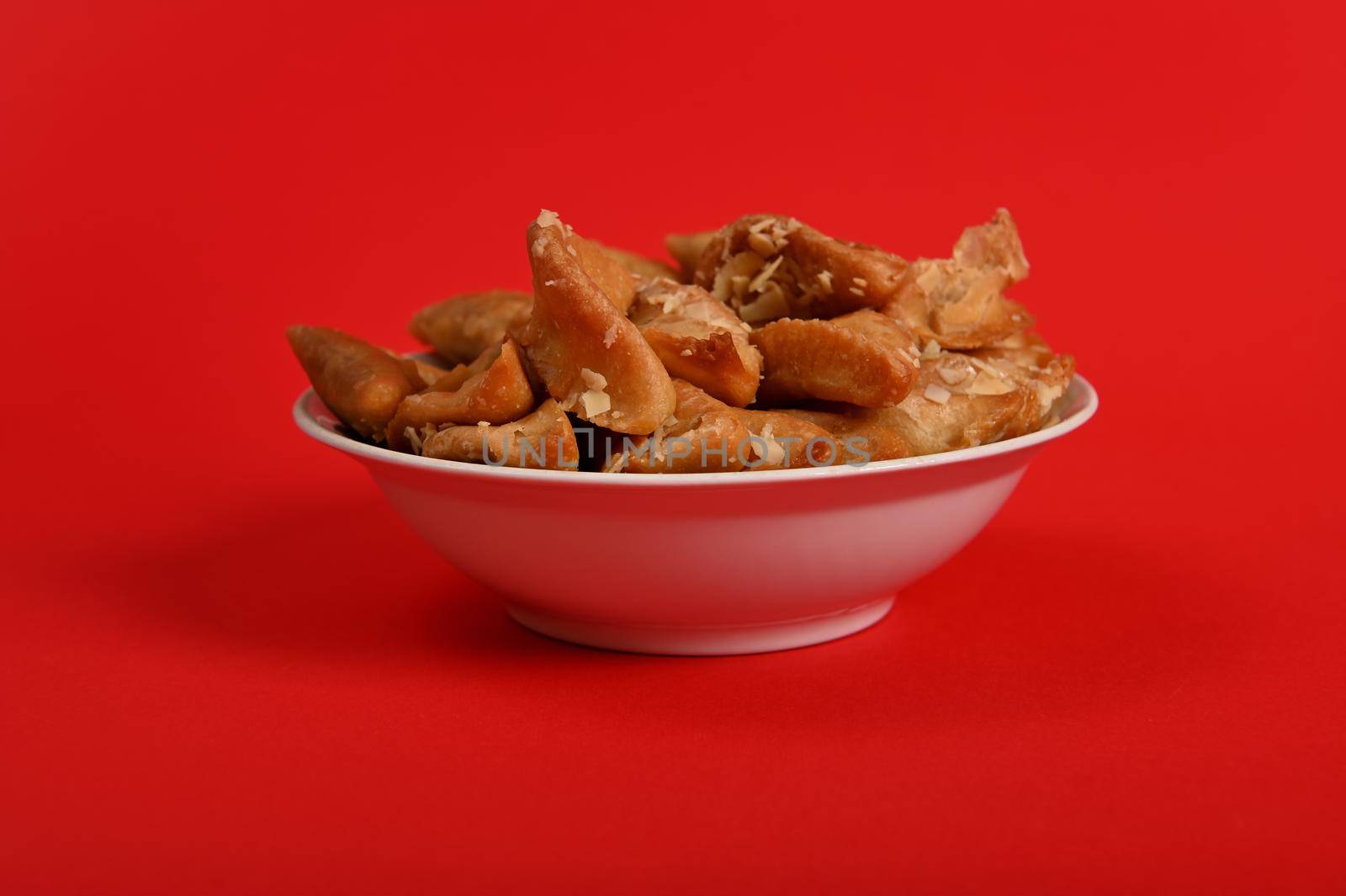 Horizontal shot of plate full of fresh traditional luxurious Arabian handmade Brewat sweets, isolated on red background with space for text