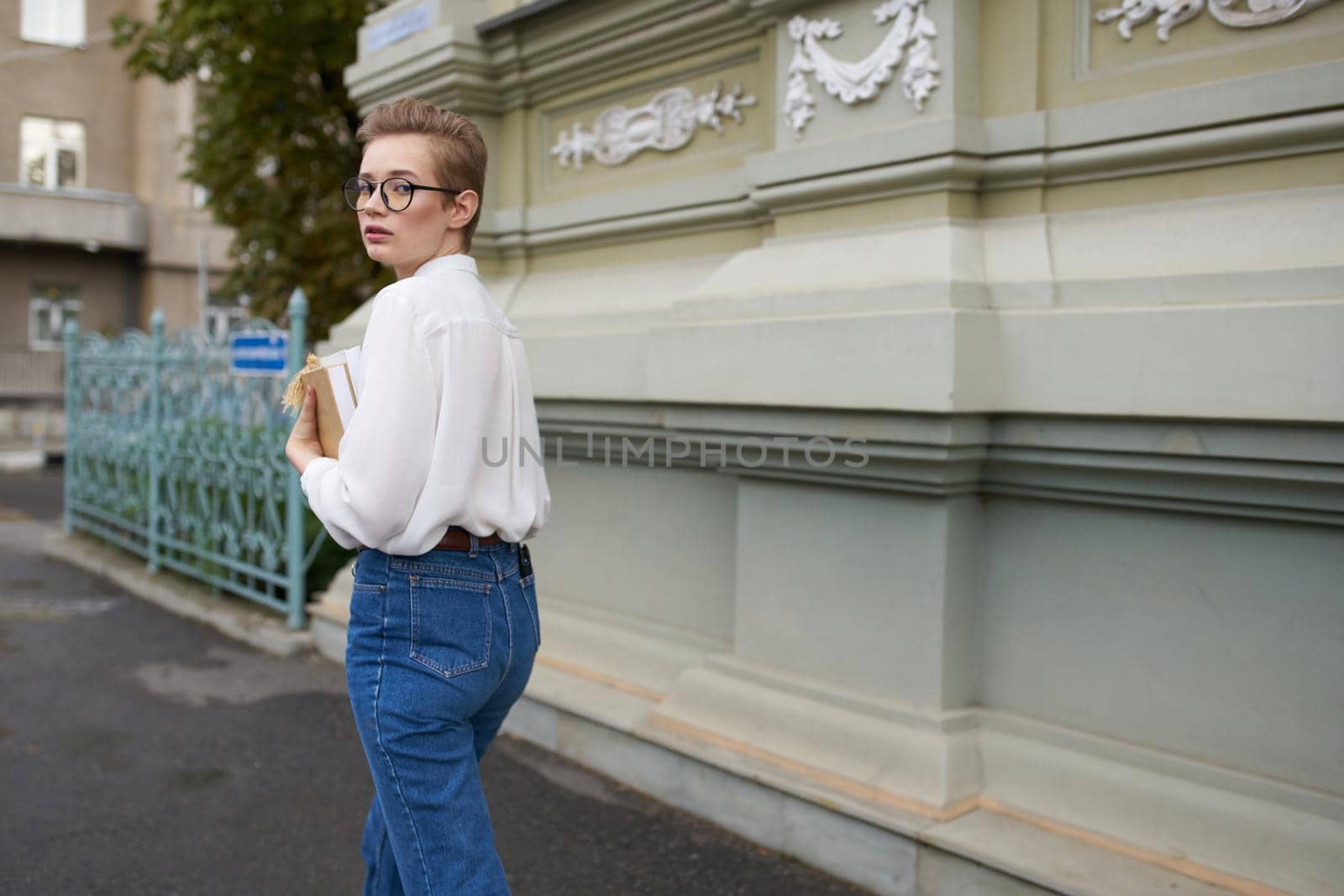 short haired woman with glasses walking around the city with a book education. High quality photo