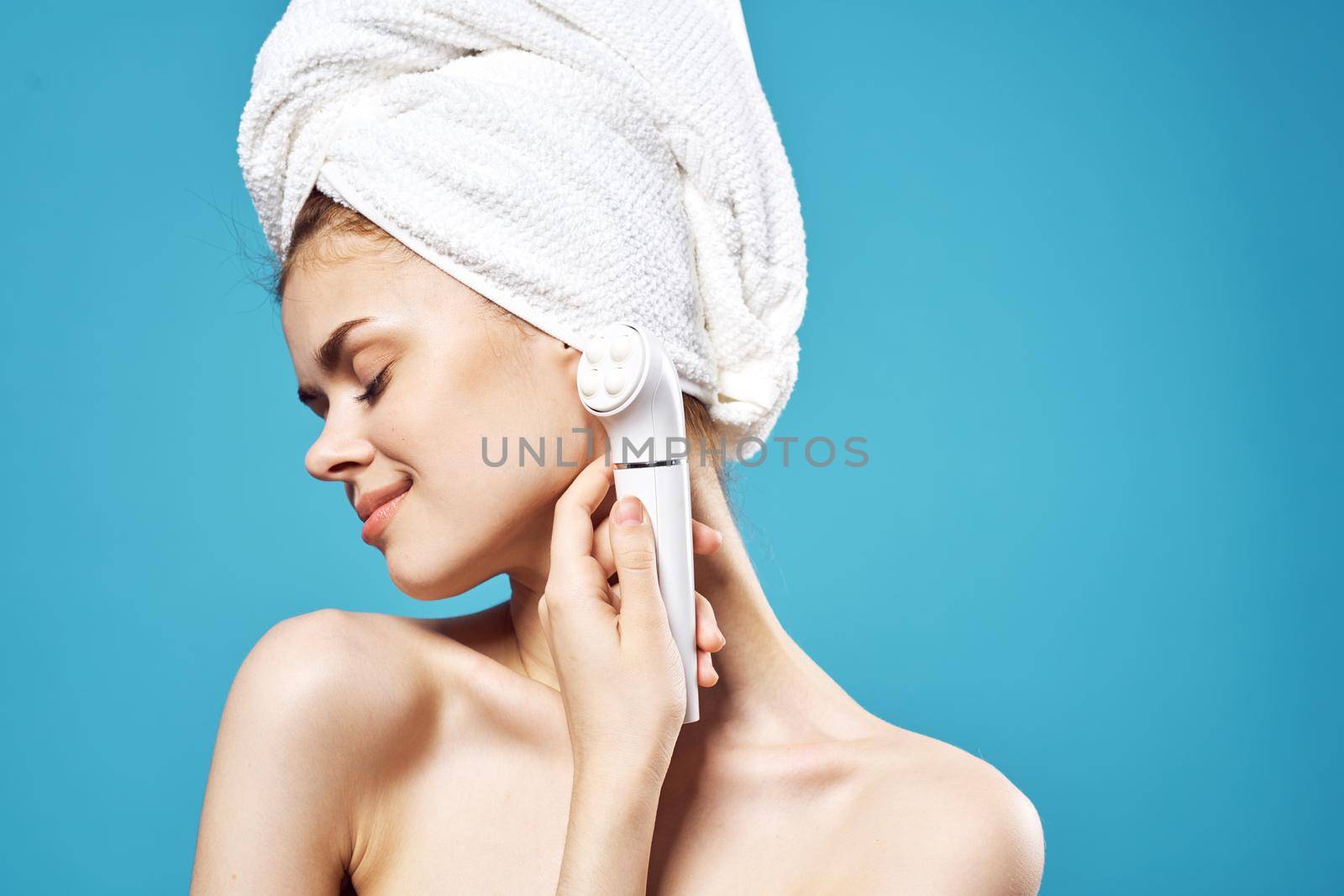 woman with bare shoulders and holding a massager in her hands for a face blue background. High quality photo