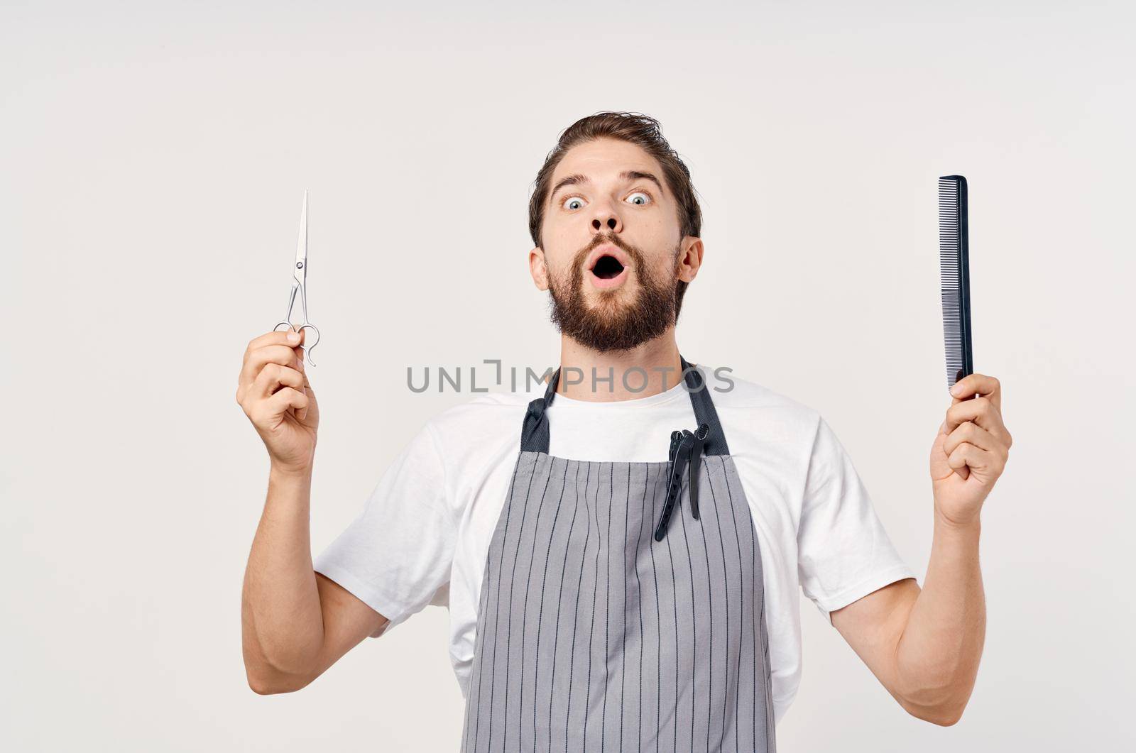 man hairdresser in a gray apron with a comb and scissors emotions light background hairstyles model. High quality photo