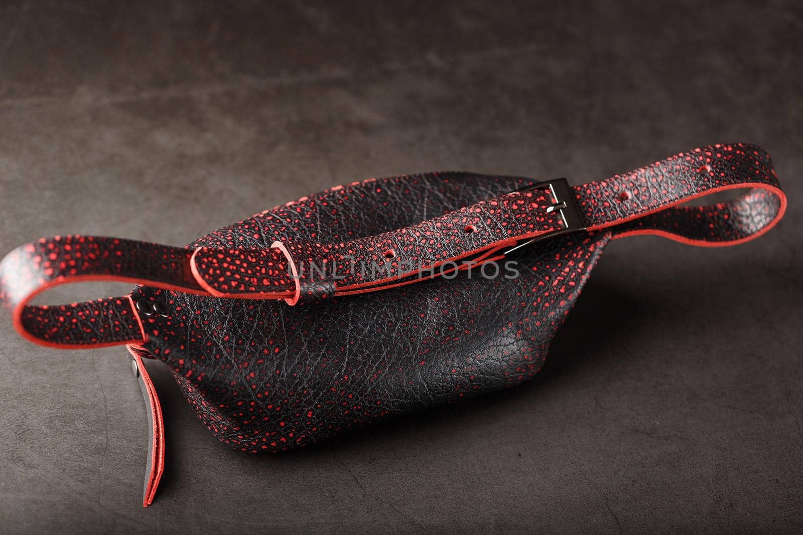 Belt bag made of textured, spotty black and red leather on a stone dark background. Elegant black and red bag with a zipper. Genuine leather, handmade. Banana bag
