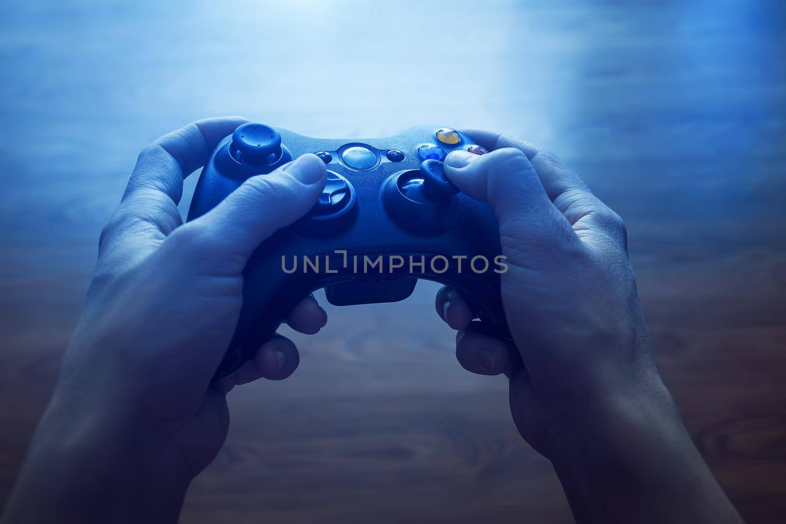 Video game controller in the hands of man. In front of the TV in the evening, with blue light from the screen