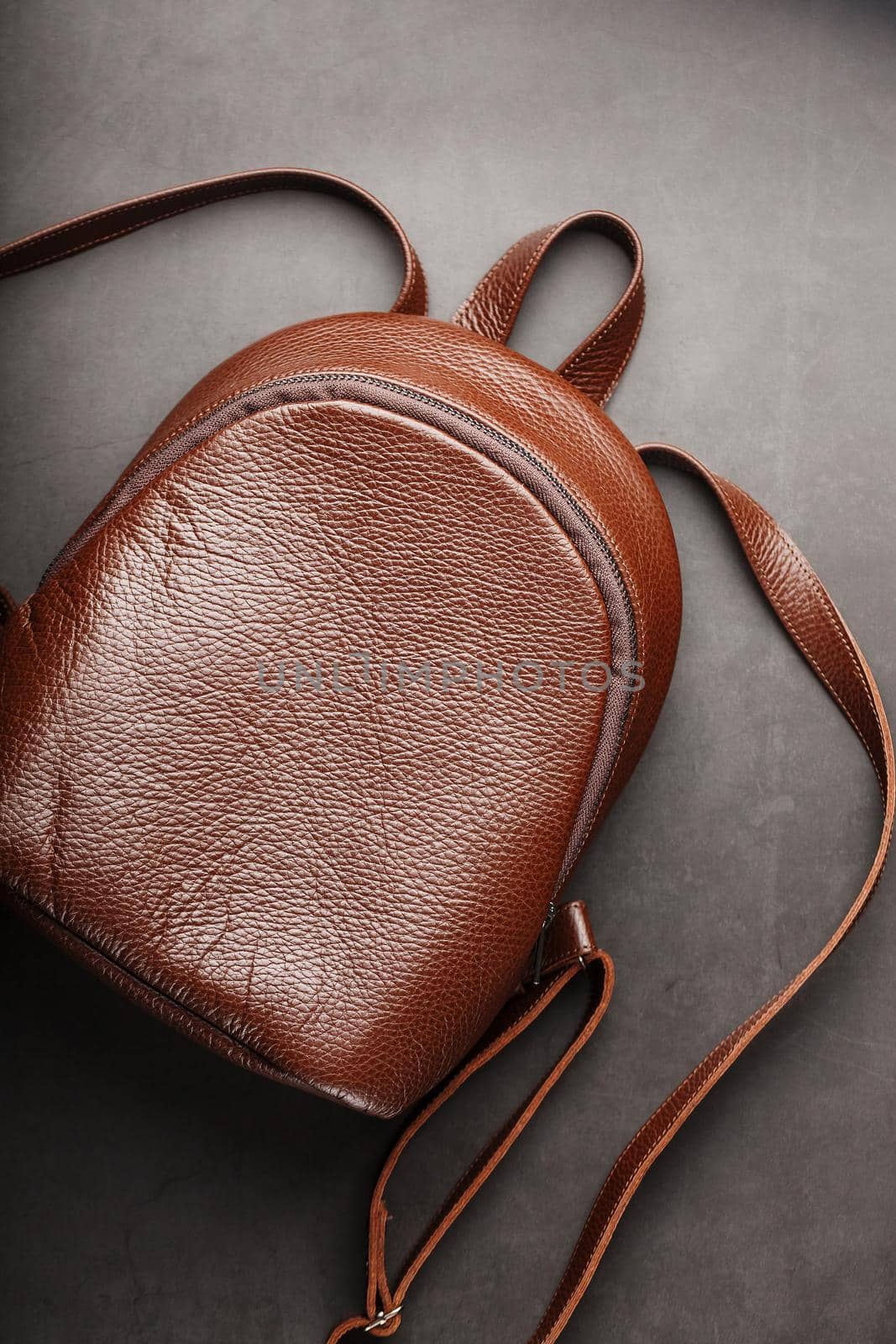 Brown backpack made of textured brown leather on a black stone background. Elegant golden brown women backpack with fashion and rivets. Genuine leather, handmade.