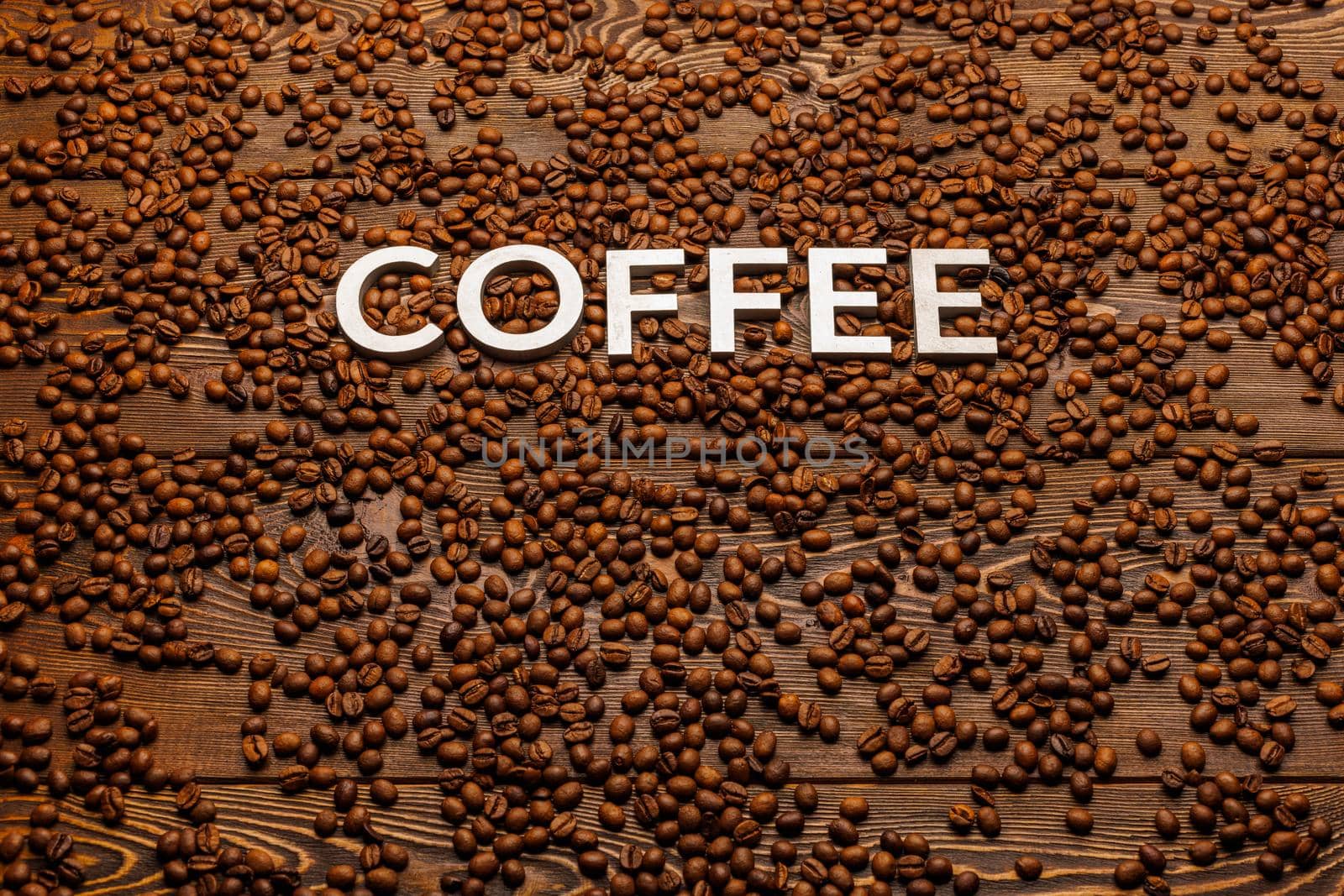 the word coffee laid with silver letters on wooden board surface covered with roasted coffee beans - close-up view with selective focus