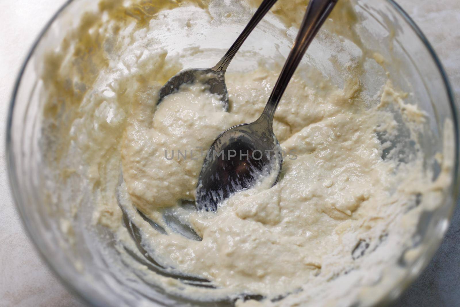 Large glass bowl with leftovers of batter and two tablespoons, close-up view from above.