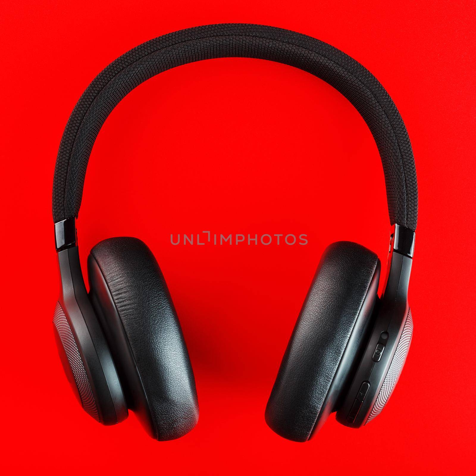 Black wireless headphones on a red background. Overhead, isolated professional-grade headphones for DJs and musicians by AlexGrec