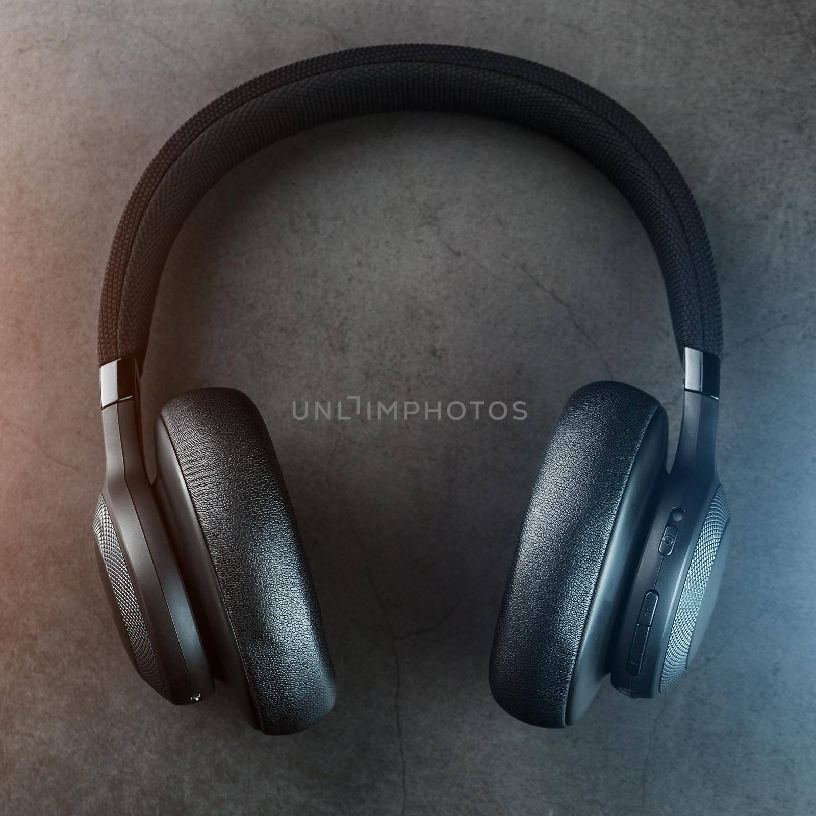 Wireless black headphones on a dark background with blue and orange backlight. On-ear headphones for playing games and listening to music tracks. Modern style