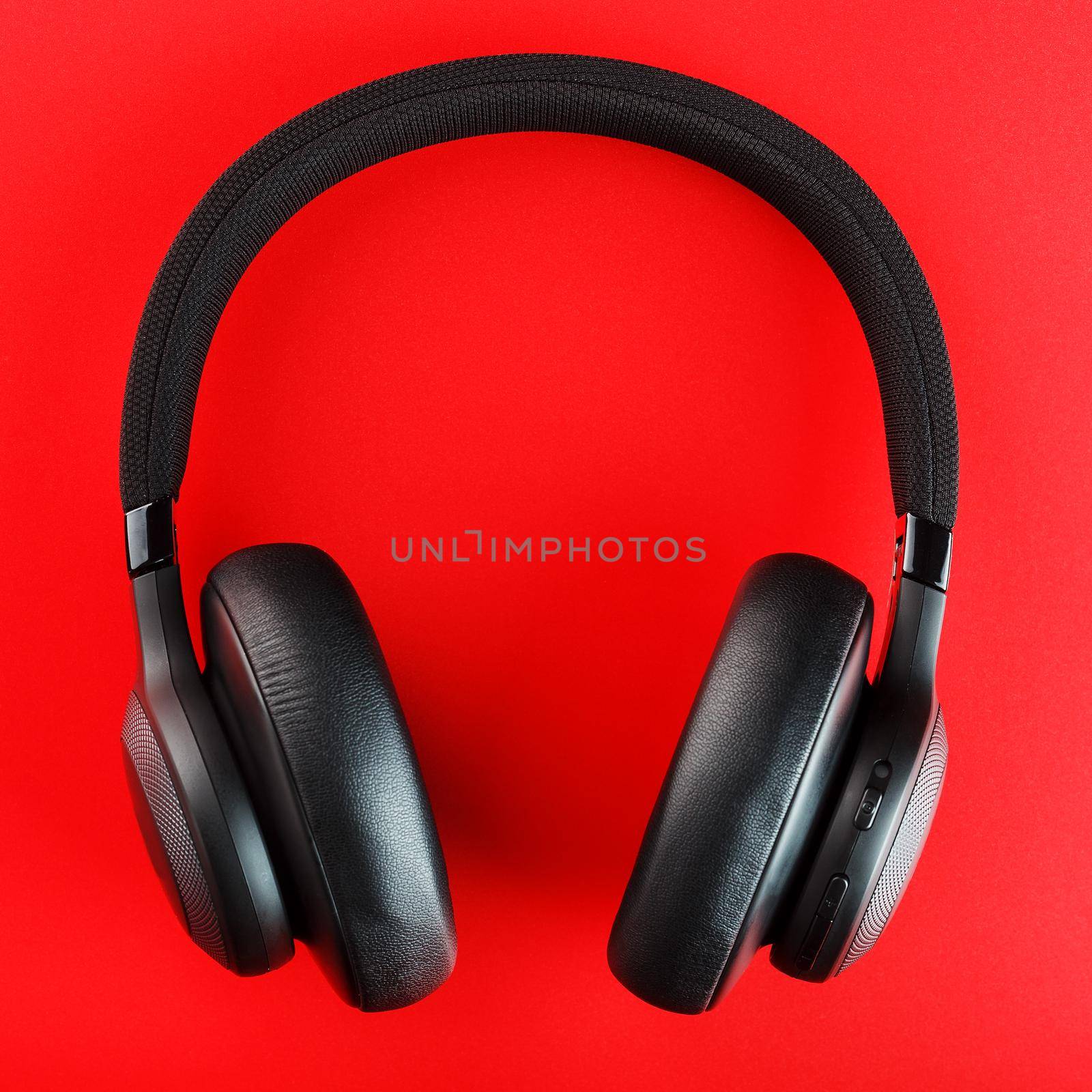 Wireless black headphones on a red background. View from above. In-ear headphones for playing games and listening to music tracks. Modern style