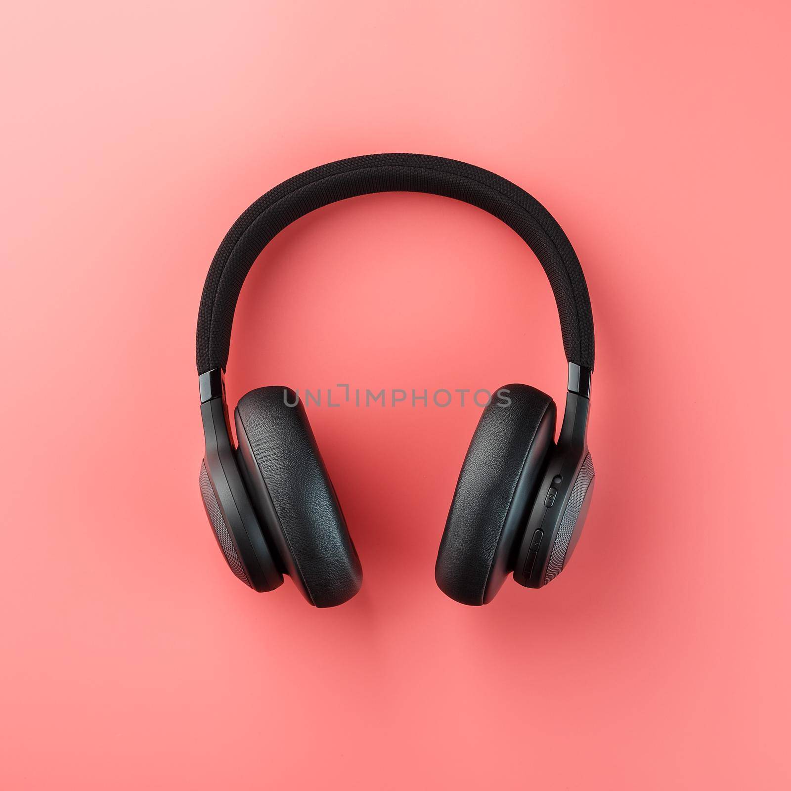 Wireless black headphones on a pink background. View from above. In-ear headphones for playing games and listening to music tracks. Modern style
