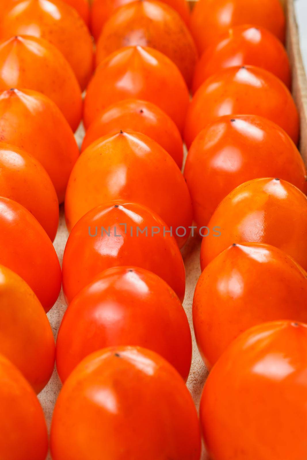 Fresh ripe persimmons in market. Persimmons background. Repeating rows of juicy, ripe persimmon in a box. Close-up, macro