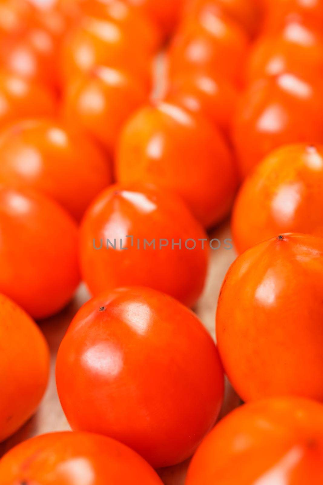 Fresh ripe persimmons in market. Persimmons background. Repeating rows of juicy, ripe persimmon in a box. Close-up, macro