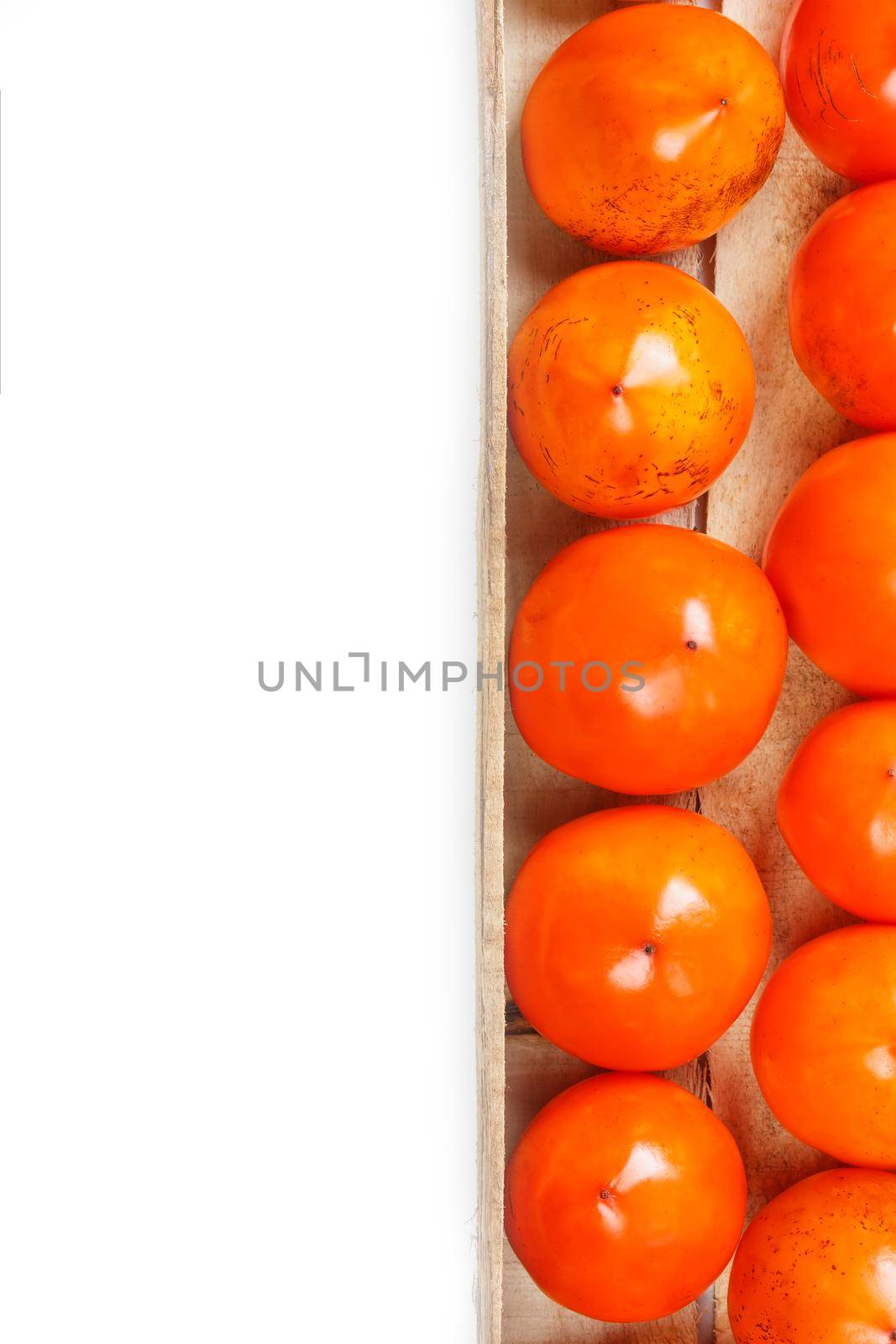 Persimmon fruit in the wooden box isolated on white. Clipping Path included. Juicy ripe persimmon in a large wooden box on a white background. The edge of a wooden box with orange persimmon and a place for text on a white background