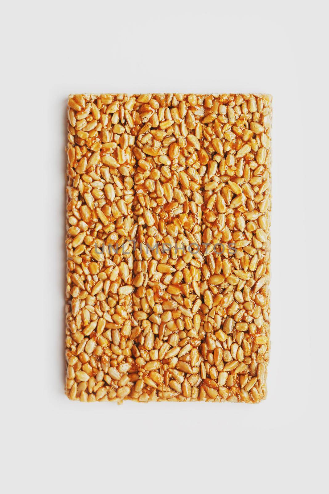 A large golden tile of sunflower seeds, a bar in a sweet molasses on a white background. Kozinaki useful and tasty sweets of the East. Top view, isolated.