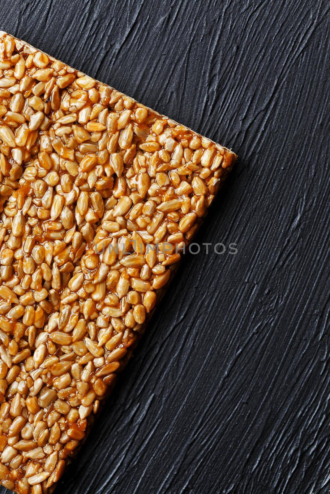 Tile kozinaki from sunflower seeds on a black textural background. Delicious oriental sweets Gozinaki from sunflower seeds, sesame seeds and peanuts, covered with honey with a shiny icing. View from above