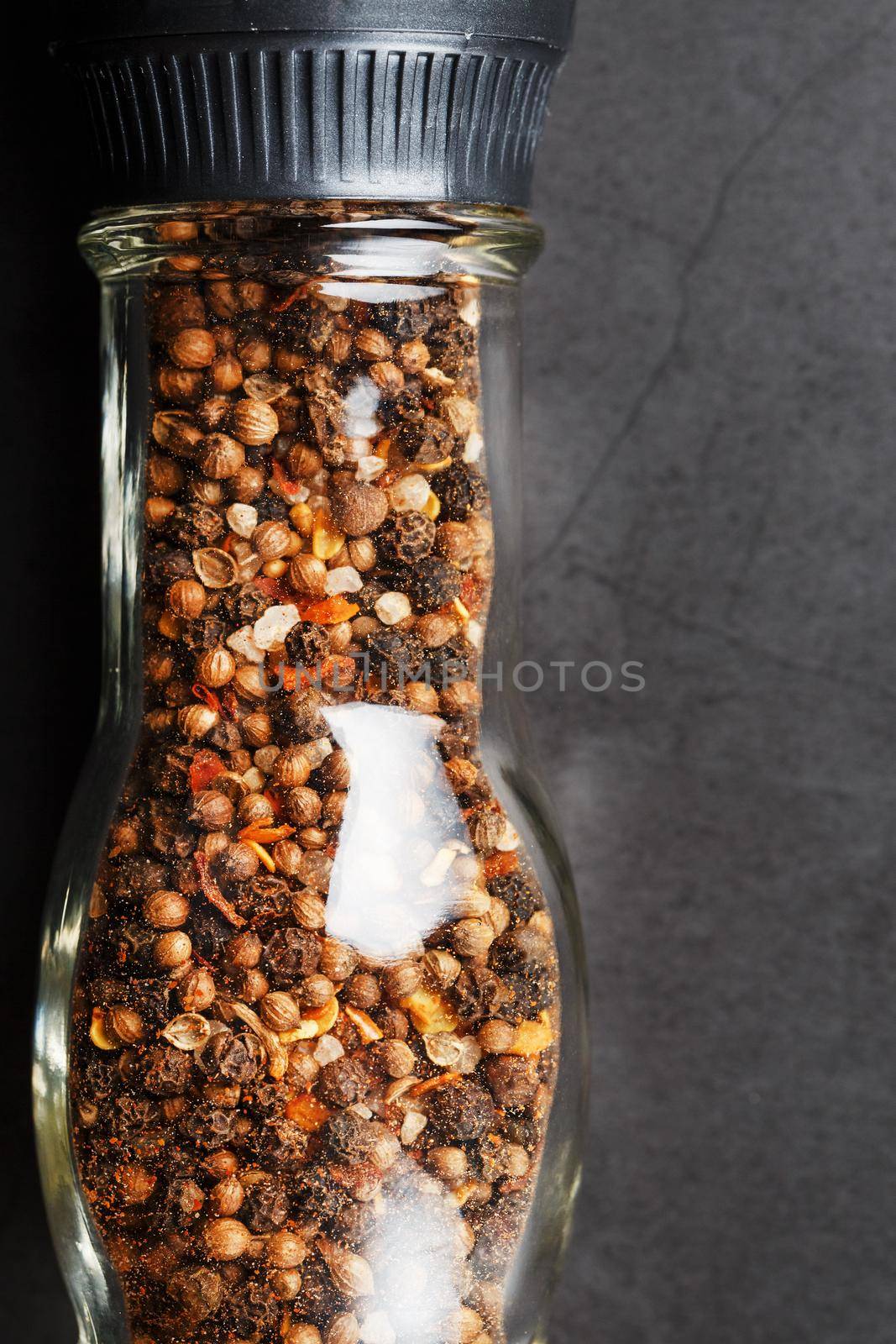 A mixture of seasonings, spices and herbs in a glass mill on a black background. Free space top view, minimalism