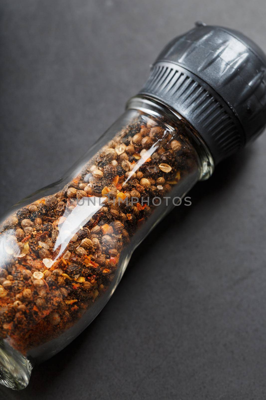 Peppercorns cumin and salt in a transparent mill on a black background
