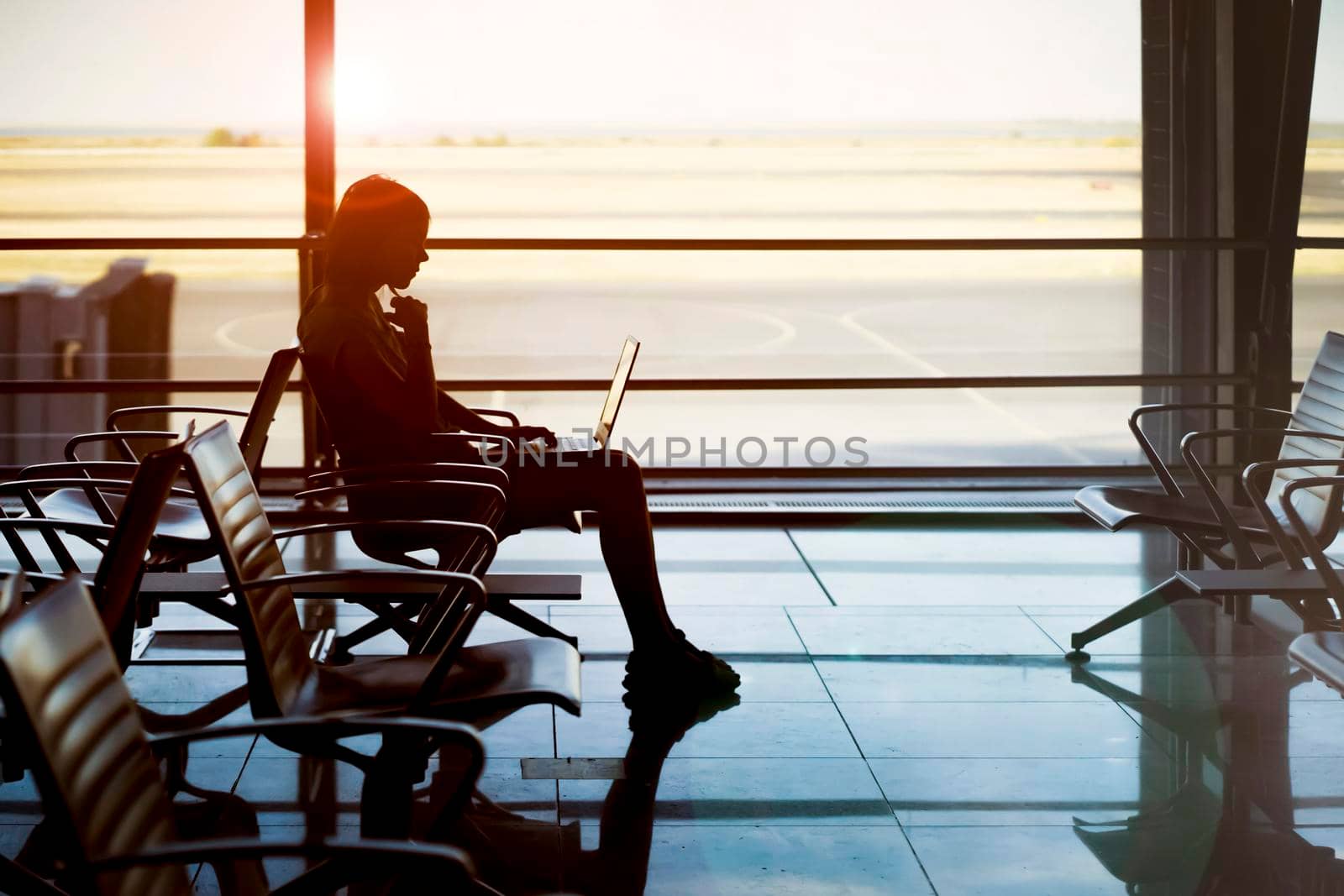 A young girl works on a laptop at the airport while she waits to board a plane. A woman buys tickets, studies and communicates via the Internet, the airport in the background.