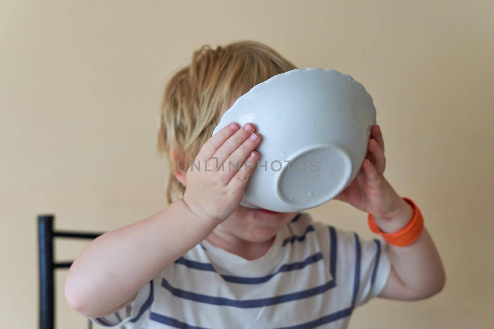 The child drinks from a plate holding it in his hands. The child eats the leftovers