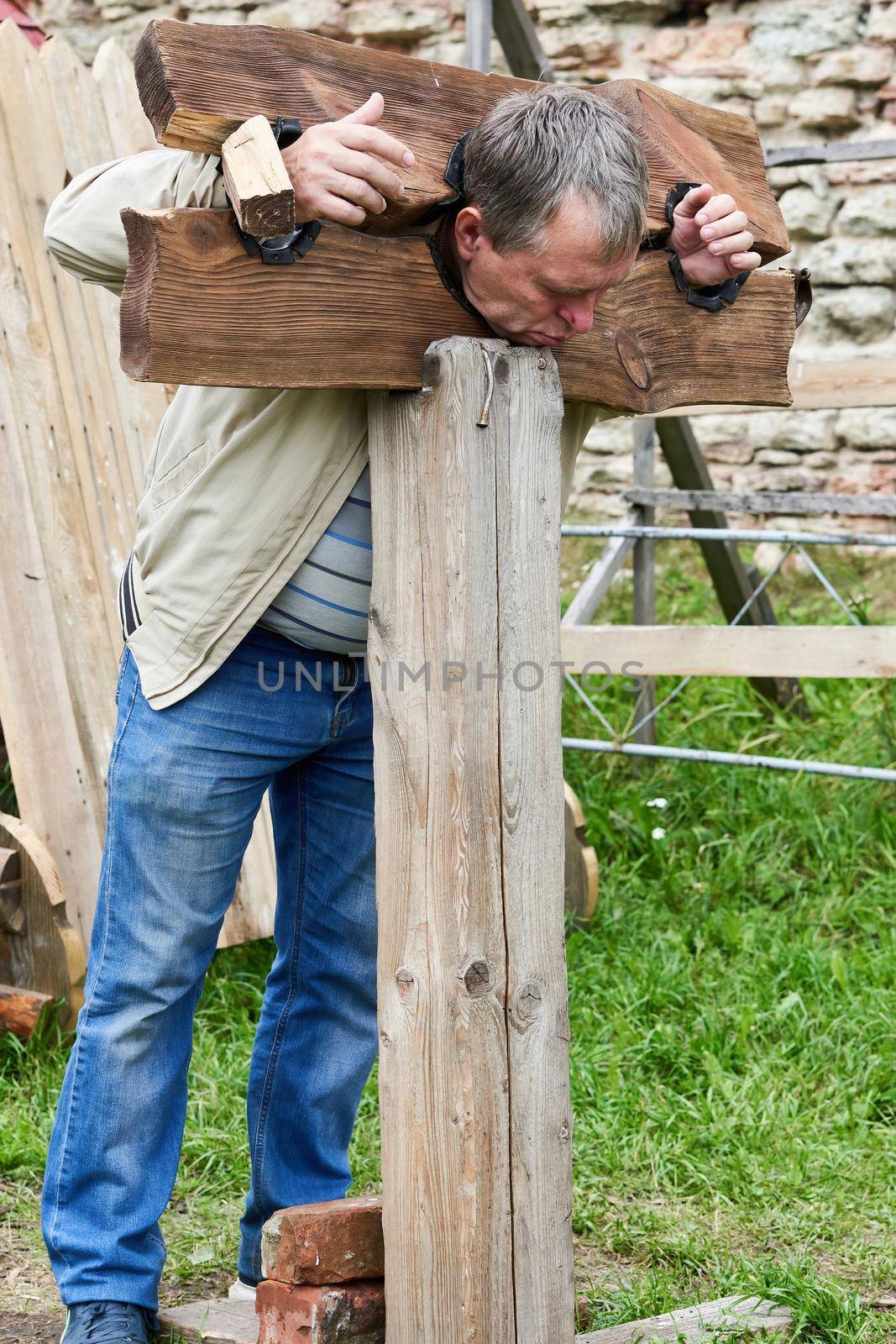Man in wooden stocks from medieval times for use with prisoners, criminals or witches as public punishment