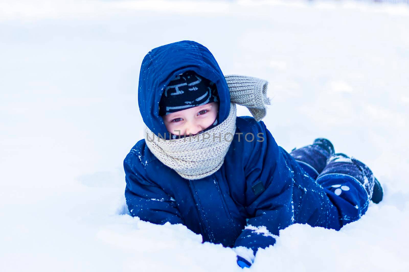 A smiling happy child lies in a snowdrift on a sunny winter day. A lot of snow and very frosty. Active winter outdoor games. The concept of a happy Christmas vacation.