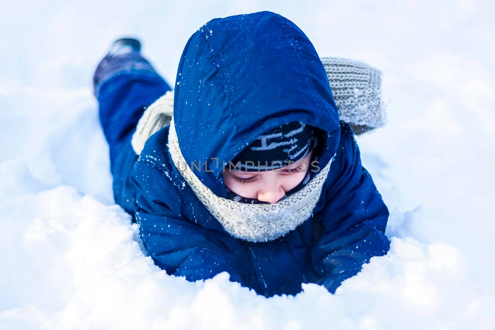 A smiling happy child lies in a snowdrift on a sunny winter day. A lot of snow and very frosty. Active winter outdoor games. The concept of a happy Christmas vacation.