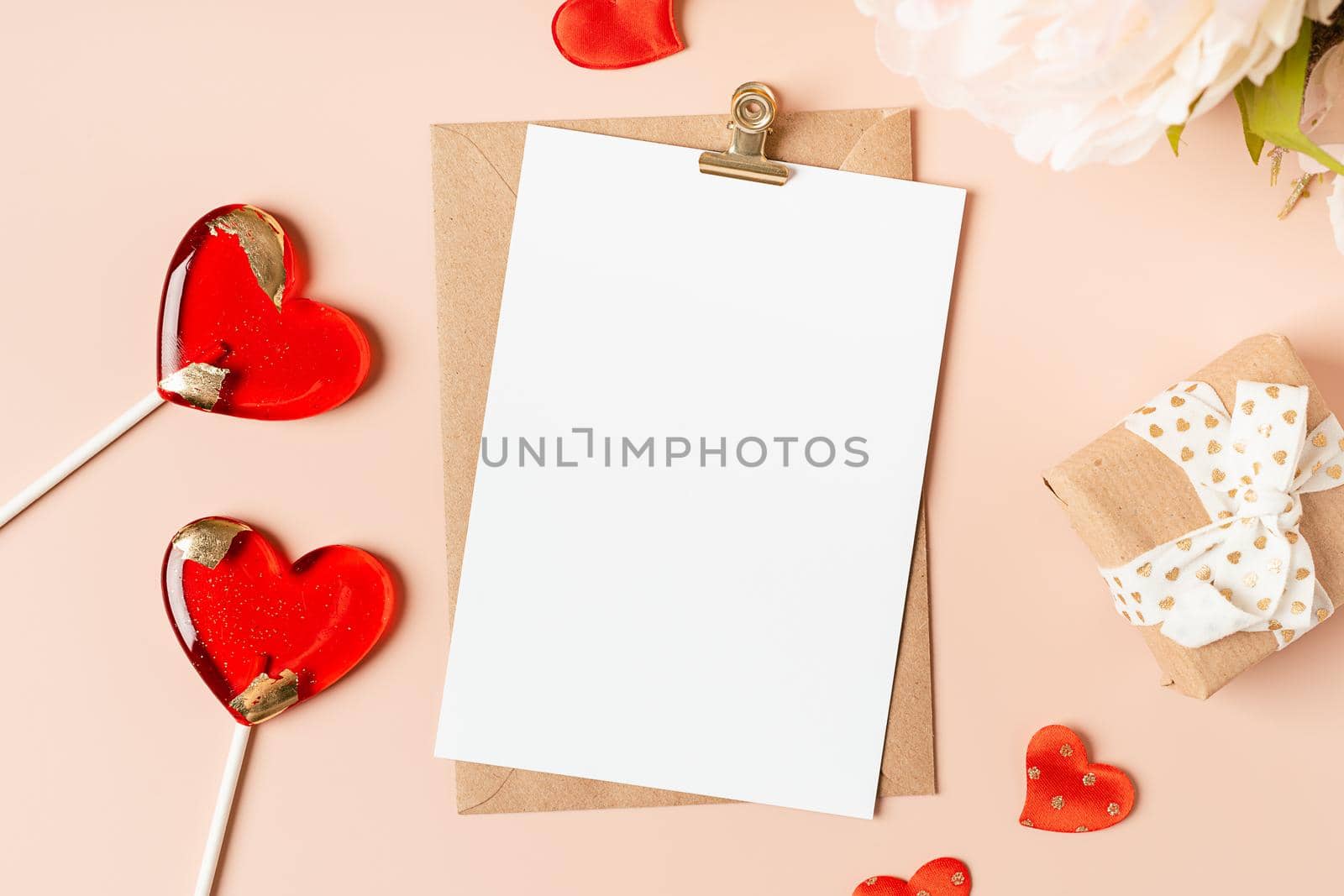 Flat lay of paper envelope with blank mockup greeting paper card. Pink table background with Valentine day gift, letter, heart shape, lollipops and decoration. Top view, mock up invitations